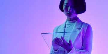 Woman interacts with a transparent digital screen in vibrant studio lighting.