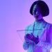 Woman interacts with a transparent digital screen in vibrant studio lighting.