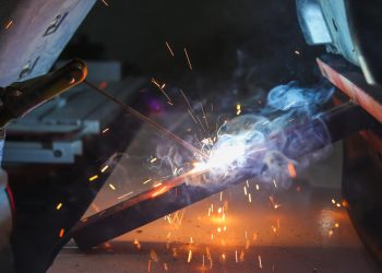 Close-up of a welder at work with sparks and smoke in an industrial setting.
