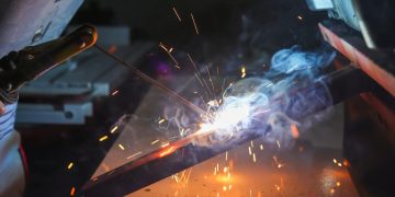 Close-up of a welder at work with sparks and smoke in an industrial setting.