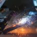Close-up of a welder at work with sparks and smoke in an industrial setting.