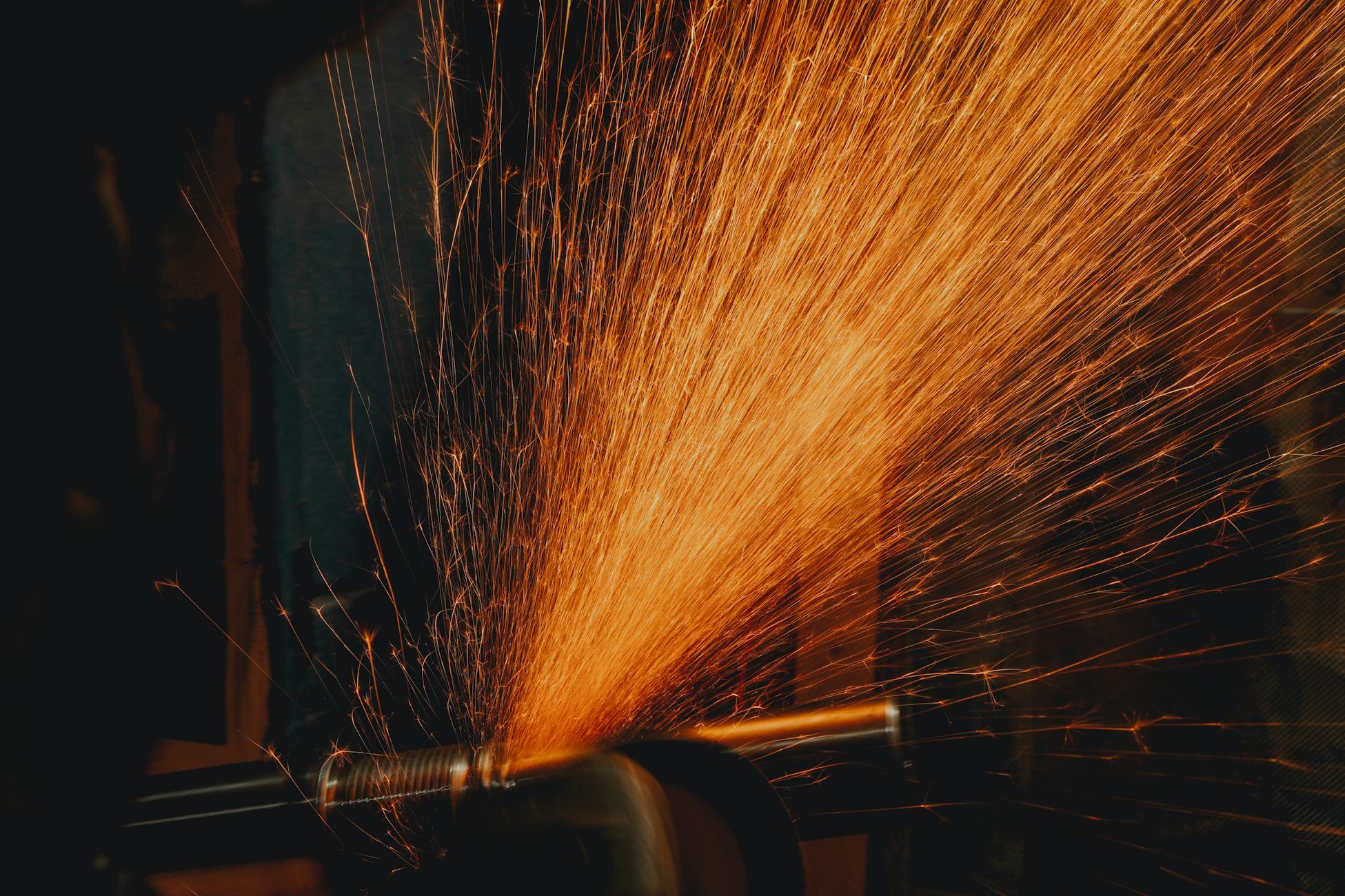 Dramatic close-up of vibrant orange sparks flying from a grinding machine, illuminating a workshop setting.