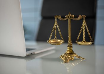 Golden justice scales on a desk beside a laptop, symbolizing law and balance.