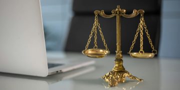 Golden justice scales on a desk beside a laptop, symbolizing law and balance.