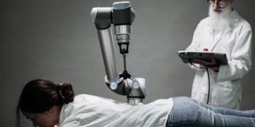 A woman receives a robotic massage as a scientist monitors, showcasing modern technology.