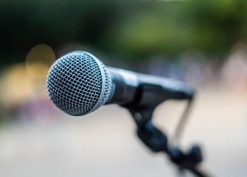 Soft focus of contemporary microphone on holder placed on stage during performance in park