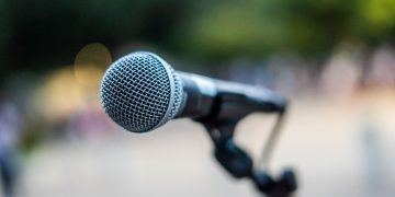 Soft focus of contemporary microphone on holder placed on stage during performance in park
