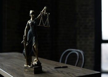 Lady Justice figurine on wooden table in dimly lit room symbolizes law and fairness.