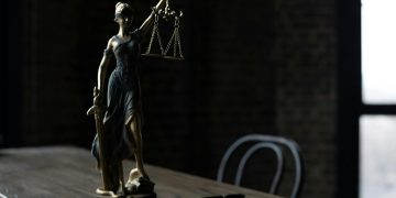 Lady Justice figurine on wooden table in dimly lit room symbolizes law and fairness.