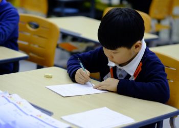 a young boy sitting at a desk writing on a piece of paper