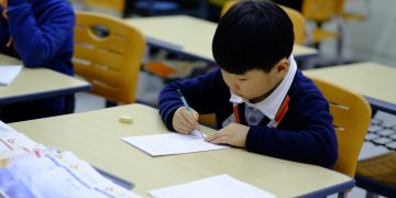 a young boy sitting at a desk writing on a piece of paper