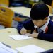 a young boy sitting at a desk writing on a piece of paper