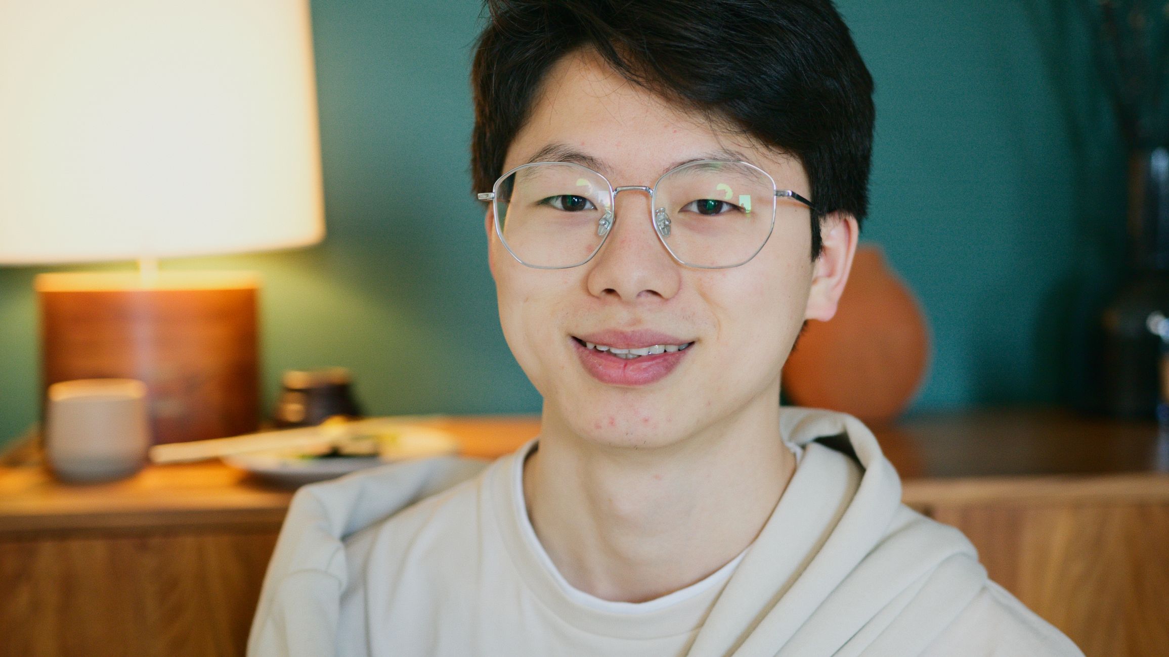 Close-up portrait of a smiling young Asian man wearing glasses, indoors.