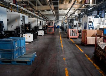 Vast industrial factory floor with machinery, crates, and structured workstations.