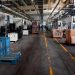 Vast industrial factory floor with machinery, crates, and structured workstations.