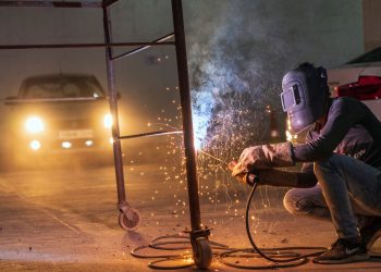 A welder at work with sparks flying in an industrial setting during night time.