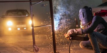 A welder at work with sparks flying in an industrial setting during night time.