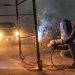 A welder at work with sparks flying in an industrial setting during night time.