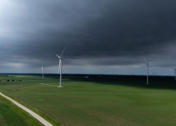 A stormy sky looms over a vast green landscape with wind turbines generating renewable energy.