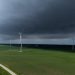 A stormy sky looms over a vast green landscape with wind turbines generating renewable energy.