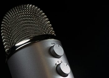 Detailed close-up of a silver mesh microphone with gain control knobs against a dark background.