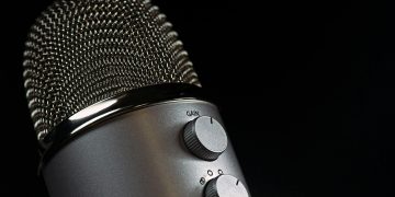 Detailed close-up of a silver mesh microphone with gain control knobs against a dark background.
