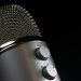 Detailed close-up of a silver mesh microphone with gain control knobs against a dark background.