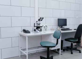 Modern laboratory with microscope, monitor, and office equipment on desk.