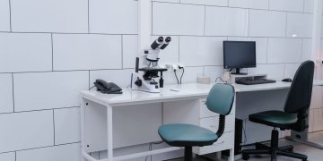 Modern laboratory with microscope, monitor, and office equipment on desk.