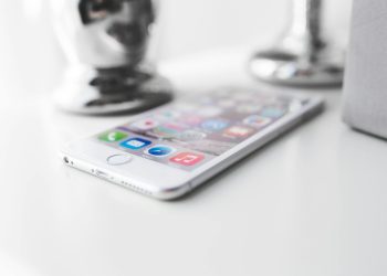 Close-up of a modern silver smartphone on a white surface with apps visible.