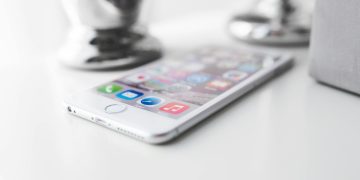 Close-up of a modern silver smartphone on a white surface with apps visible.