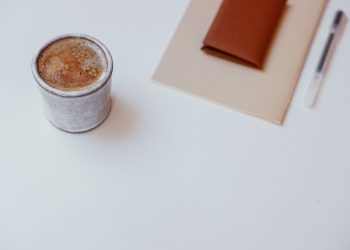 A minimalist setup with a cup of coffee, a notebook, and a pen on a white tabletop.