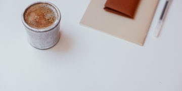 A minimalist setup with a cup of coffee, a notebook, and a pen on a white tabletop.