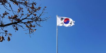 South Korean flag on a flagpole against a vibrant blue sky with tree branches.