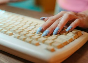 Closeup of a hand with polka dot nails typing on a vintage keyboard, emphasizing retro technology.