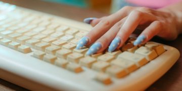 Closeup of a hand with polka dot nails typing on a vintage keyboard, emphasizing retro technology.