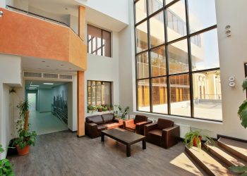 A spacious, modern lobby with high ceilings, large windows, and contemporary furniture.
