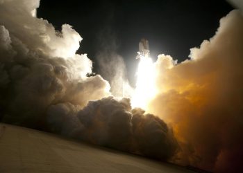 A dramatic image of a space shuttle launching into the night sky, surrounded by billowing smoke and intense light.