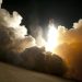 A dramatic image of a space shuttle launching into the night sky, surrounded by billowing smoke and intense light.