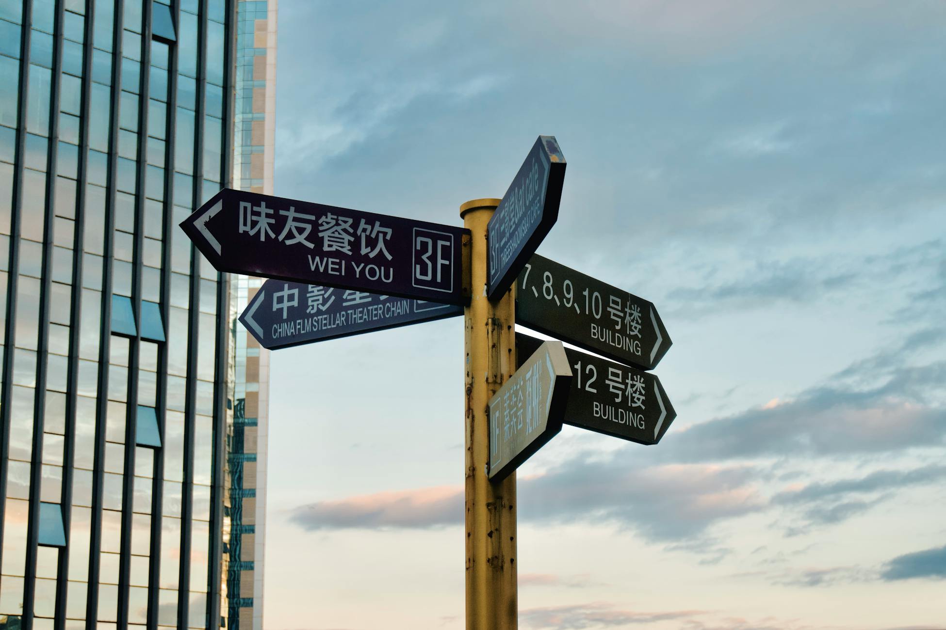 Direction signs in urban area with skyscraper backdrop at sunset.