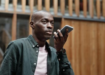 Stylish adult man using his smartphone for voice commands in an outdoor urban setting.