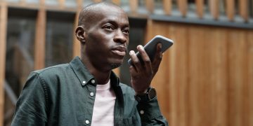 Stylish adult man using his smartphone for voice commands in an outdoor urban setting.