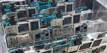 From above of circuit boards of modern smartphones placed in plastic box in electronics factory