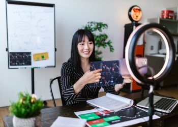 Asian woman discussing cryptocurrency investment during a vlogging session with charts.
