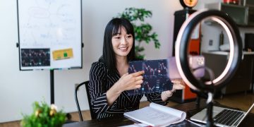 Asian woman discussing cryptocurrency investment during a vlogging session with charts.