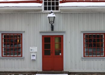 Historic wooden house with red doors and snow on the roof, embodying a wintery charm.