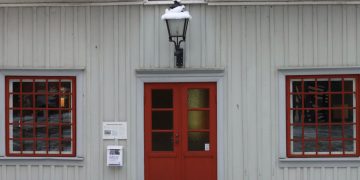 Historic wooden house with red doors and snow on the roof, embodying a wintery charm.