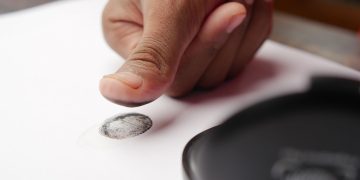 Detailed shot of a thumb creating a fingerprint on white paper, ideal for security themes.