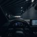 View from car dashboard driving through an illuminated city tunnel at night.