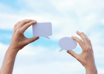 Close-up of hands holding speech bubbles, symbolizing communication and dialogue against a blue sky.